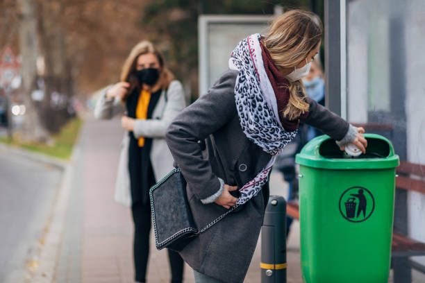Responsible woman throw away her disposable coffee cup at the trash bin while waiting for her bus at the bus station