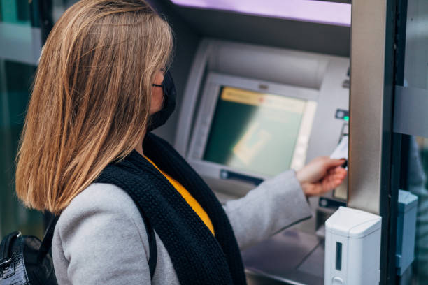 istock Woman inserting an credit card into ATM machine, while wearing protective face mask for her safety due COVID-19 pandemic 1291075161