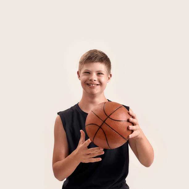 istock Cheerful disabled boy with Down syndrome smiling at camera, playing with basketball while posing isolated over white background 1291075166