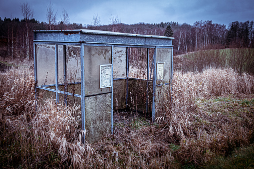 Old overgrown and weathered abandoned bustop in rural landscape