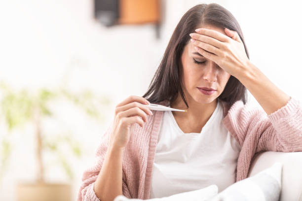 istock Woman holds her forehead while measuring temperature at home. 1291077995