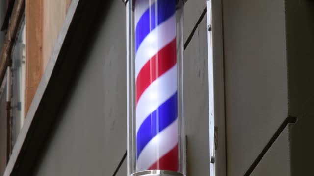 Barber pole rotating on old wall of hairdresser shop