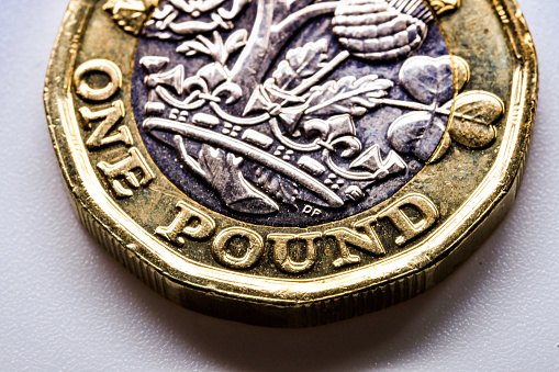 Close up of the edge of a one pound coin. The face of the coin has the symbols of the constituent countries of the UK. No people. Copy space.