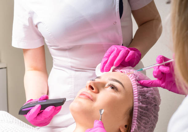 Two cosmetologists working with face of a patient at the same time