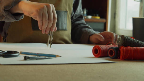 istock A tailor in an apron makes a marking with compasses on the pattern. In the foreground, reels with colored threads 1291082460