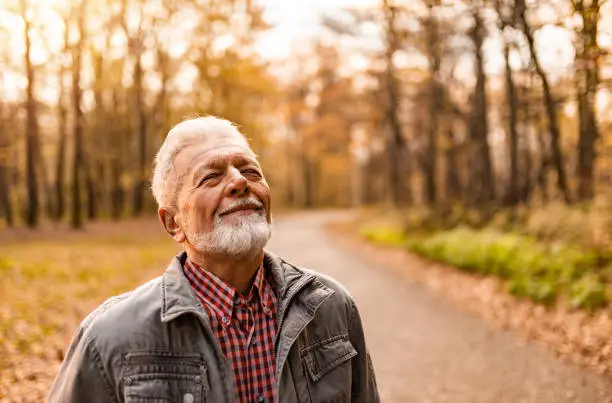Tranquil senior man enjoying a walk on forest road on autumn day and breathing fresh air with eyes closed.