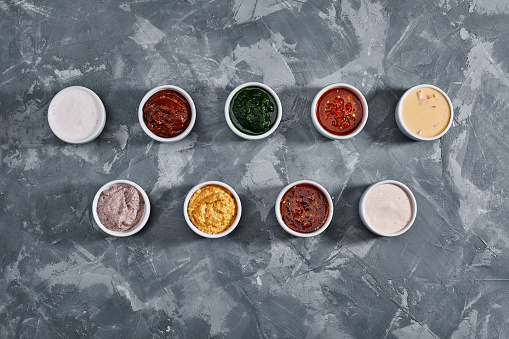 Different tasty sauces in bowls, various sauces on gray stone background, top view.