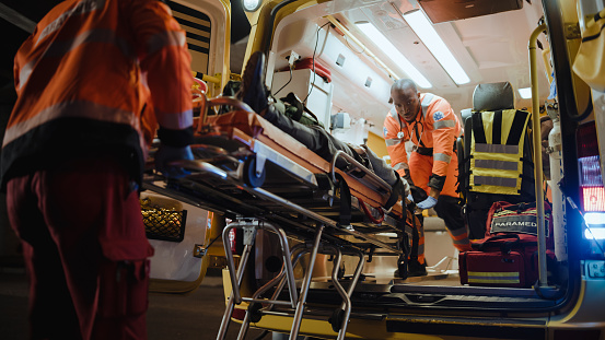 Equipo de paramédicos de EMS reaccionan rápido para llevar al paciente herido al hospital de atención médica y sacarlo de la ambulancia en una camilla. Los asistentes de atención de emergencia ayudan al joven a mantenerse vivo después del accidente. photo