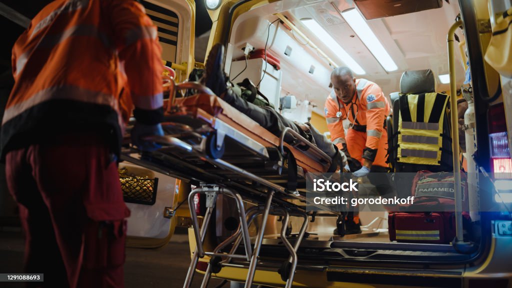 Team of EMS Paramedics React Quick to Bring Injured Patient to Healthcare Hospital and Get Him Out of Ambulance on a Stretcher. Emergency Care Assistants Help Young Man to Stay Alive After Accident. Ambulance Stock Photo