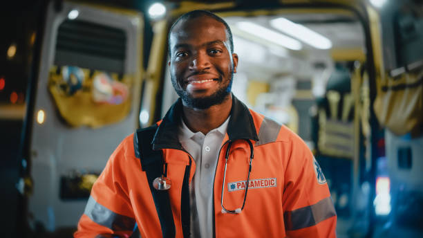 Portrait of a Black African American EMS Paramedic Proudly Standing in Front of Camera in High Visibility Medical Orange Uniform and Smiling. Successful Emergency Medical Technician or Doctor at Work. Portrait of a Black African American EMS Paramedic Proudly Standing in Front of Camera in High Visibility Medical Orange Uniform and Smiling. Successful Emergency Medical Technician or Doctor at Work. paramedic stock pictures, royalty-free photos & images