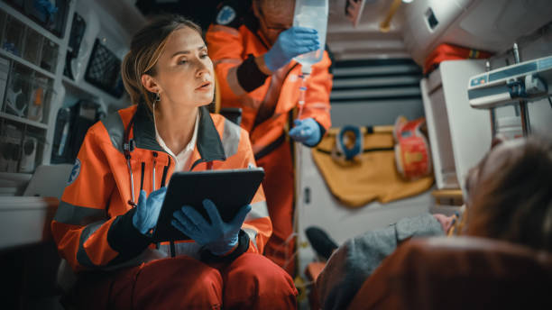 paramédico profesional de ems femenina usando tablet computer para llenar un cuestionario para el paciente lesionado en el camino al hospital. asistente de atención de emergencias para consolar al paciente en una ambulancia. - técnico en urgencias médicas fotografías e imágenes de stock