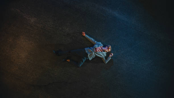 top down shot of a bloody man lying on the pavement after accident on a street at night. young man was shot and lies unconscious. concept of horrbile murder with death. - crime scene chalk outline crime murder imagens e fotografias de stock