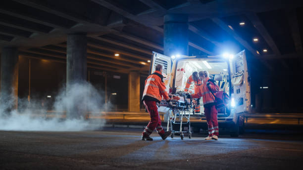 il team di paramedici ems reagisce rapidamente per portare il paziente ferito all'ospedale sanitario e portarlo fuori dall'ambulanza su una barella. gli assistenti alle cure di emergenza aiutano il giovane a rimanere in vita dopo l'incidente. - emergency services and rescue occupation foto e immagini stock