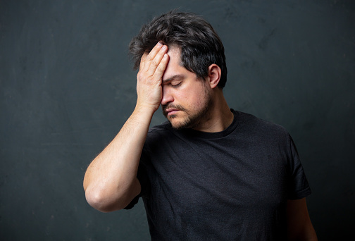 Tired brunet man in black t-shirt on dark background