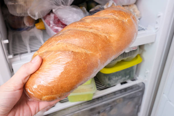 a hand putting a loaf of wheat bread in reserve on a shelf of a home freezer, long life food storage concept - vegan food still life horizontal image imagens e fotografias de stock