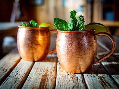 A Moscow Mule Cocktail in a rustic copper mug, perfectly garnished with mint and lime sits on a weathered wooden table.