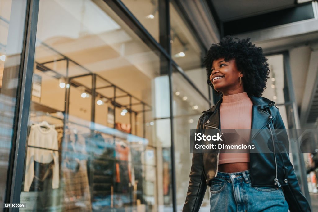 A young woman out shopping in the city A young woman out shopping in the city. Afro female standing in front of boutique and looking in the shop window Retail Stock Photo