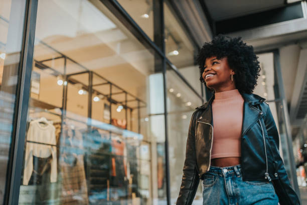 A young woman out shopping in the city A young woman out shopping in the city. Afro female standing in front of boutique and looking in the shop window retail stock pictures, royalty-free photos & images