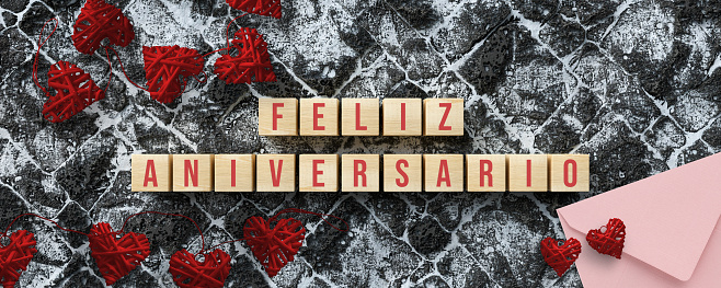 cubes with Spanish message for HAPPY ANNIVERSARY with heart shaped decoration on snowy lava stone background