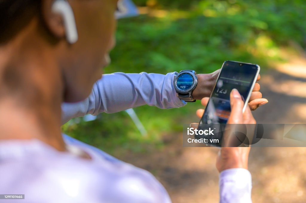 Over shoulder view on woman using tracker software Over shoulder view on Black sport woman using tracker software on smartphone and smartwatch. Modern technology and healthy lifestyle concept. Smart Watch Stock Photo