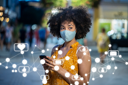 Young woman wearing protective face mask using smart phone. Social media concept.