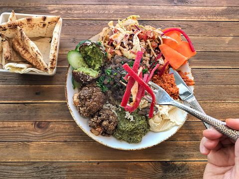 Vegan assortment of traditional Lebanese cuisine (cooked and raw) including falafel (chickpeas), fattoush (salad), mohammara (roasted red pepper dip), hummus (chickpeas), spinach dip, makali (cauliflower in pomegranate molasses), and mujadara (bean and lentil stew) with pita bread.