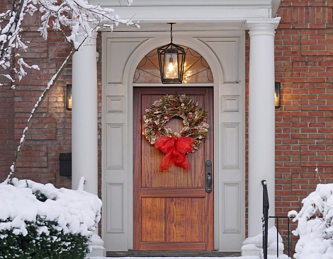 Elegant wood grain front door with Christmas wreath and snow covered trees