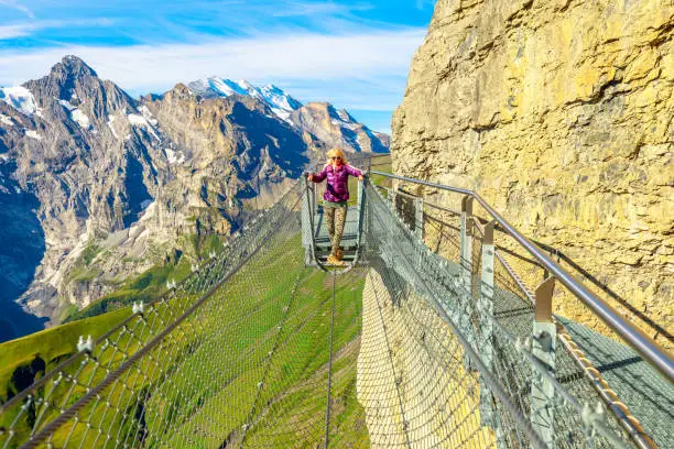 Thrill walk on Schilthorn, Bernese Prealps, Canton of Bern in Switzerland. Happy tourist woman walks on a net between high rock faces at mid-station Birg, 2677, above village of Murren.