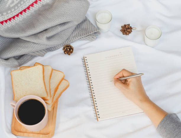 istock woman's hand is writing paper with coffee cup and bread on white background. coffee top view.  morning relaxing time winter concept. 1291119905