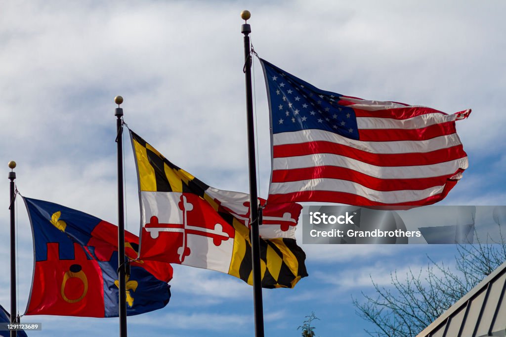 Flags of the USA, state of Maryland and Montgomery County Threeflags are vawing on seperate flags poles against blue sky on a windy day. From right to left they stand for: USA, state of Maryland and Montgomery County Maryland - US State Stock Photo