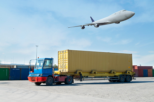 Carrying container in a commercial dock and cargo airplane flying over truck.