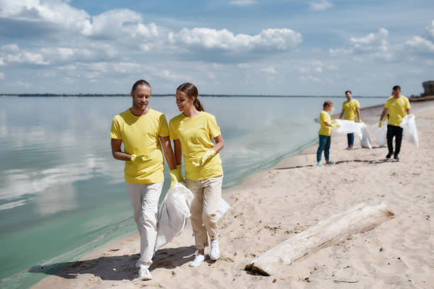 istock Two young eco activists in uniform and rubber gloves discussing something while cleaning the beach with group of volunteers 1291129839
