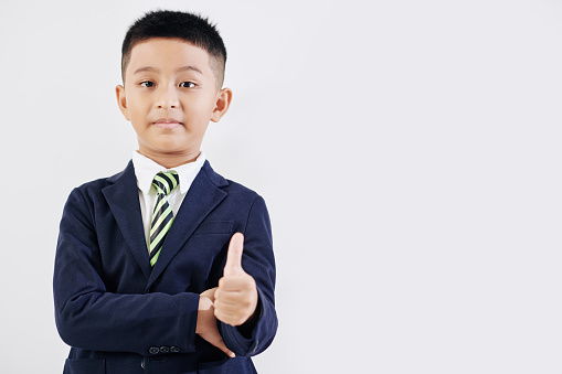 Happy schoolboy in school uniform showing thumbs-up, isolated on white