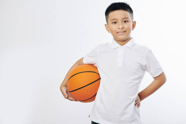 Portrait of cheerful Asian preteen boy posing with basketball ball and looking at camera