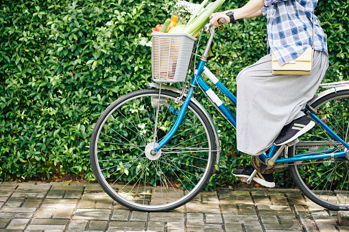 Cropped image of woman riding bicycle with basket of fresh groceries