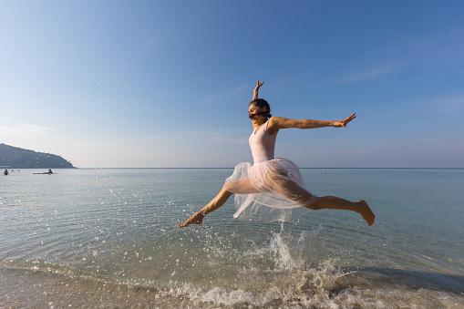 Asian woman in white dress ballet dancing on the beach.