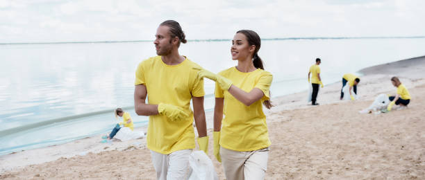 istock No more plastic. Two young eco activists in uniform and rubber gloves discussing something while cleaning beach from plastic waste with group of volunteers 1291133473