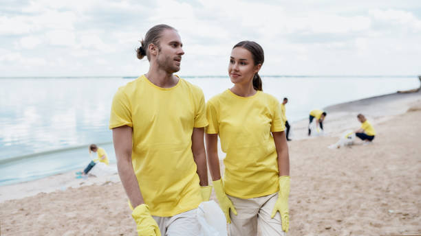 istock Save the ocean. Two young eco activists in uniform and rubber gloves discussing something while cleaning beach from plastic waste with group of volunteers 1291134506