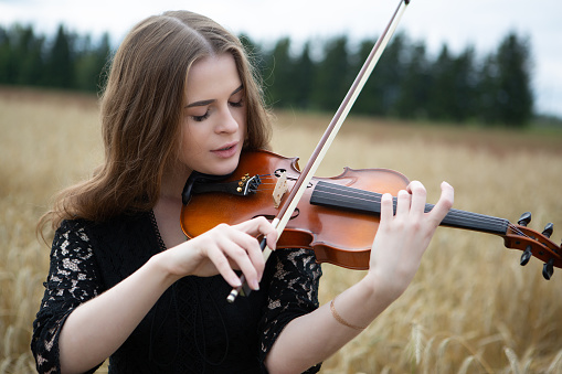 Close-up portrait of a young woman with a slight smile and downcast eyes who plays the violin in a wheat field.