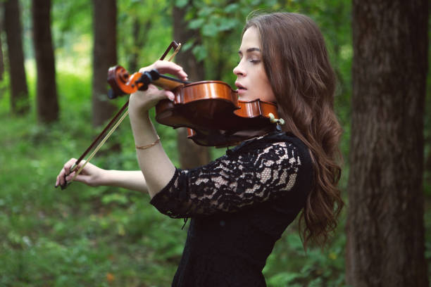 jeune femme triste jouant la pièce romantique de violon dans le parc parmi les arbres - fashion fine art portrait young adult beautiful people photos et images de collection