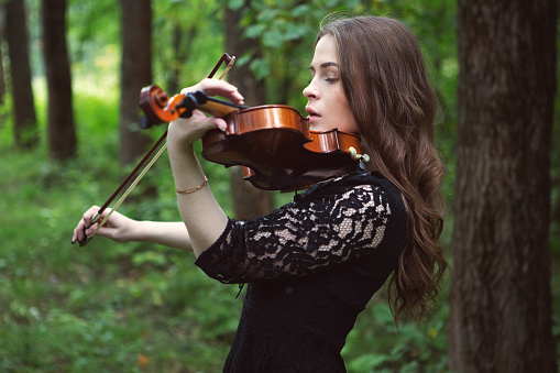 sad young woman playing the violin romantic piece in the Park among the trees