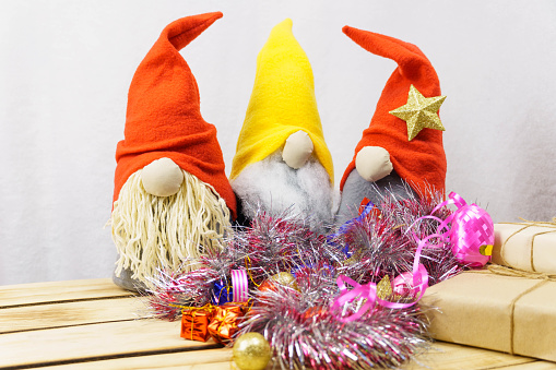 Close-up of homemade Christmas gnomes against a white background surrounded by sparkling New Year decorations.