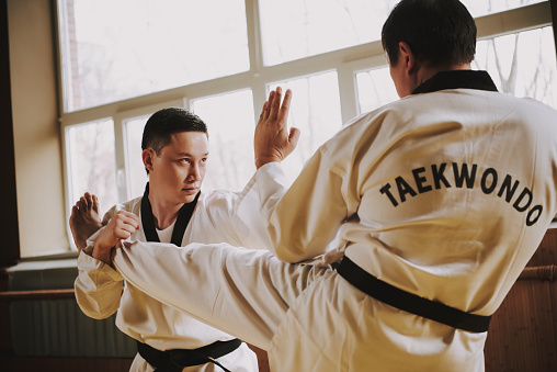 Two martial arts students in white keikogi with black belts sparring together.
