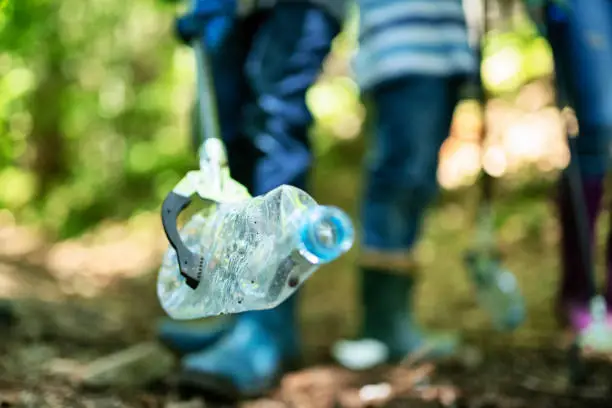 Mother and three kids cleaning up the forest. Closeup of plastic bottle held by garbage pliers.
Nikon D850