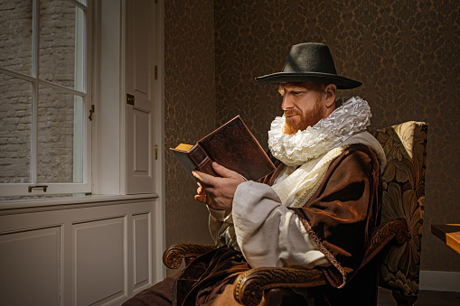 Handsome redhead traditional dutch man wearing historically correct outfit by candlelight in a typical townhouse drawing room