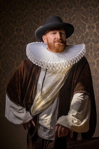 Handsome redhead traditional dutch man wearing historically correct outfit by candlelight in a typical townhouse drawing room