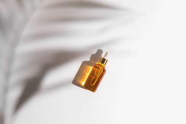 istock White, orange and black serum bottles on white background. Trending shadow from a palm branch. Cosmetic mockup. Place to insert text, images. Top view. Flat lay. 1291167032