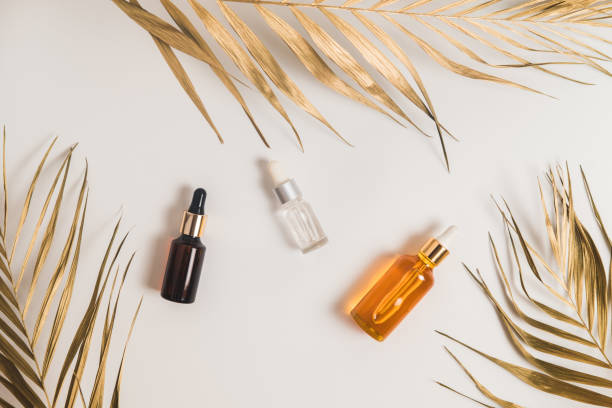 White, orange and black serum bottles on white background. Trending golden branches of palm. Cosmetic mockup. Place to insert text, images. Top view. Flat lay. stock photo