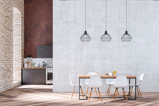 Industrial large modern kitchen with brown wooden kitchen cabinets on white tiled and high rusty wall background. An arched window on orange brick wall and pendant lights over a full dining table with white modern chairs in front of large empty concrete wall background with copy space on hardwood floor. 3d rendered image.