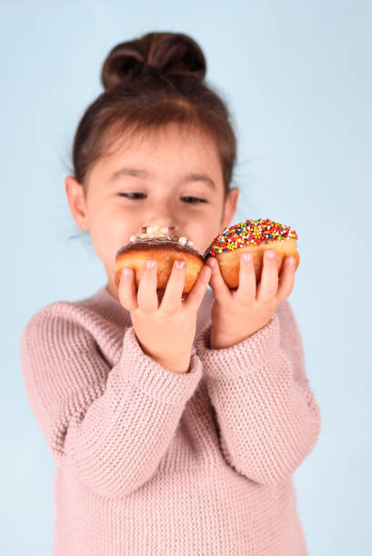 istock Little happy cute girl eating donuts on blue background 1291170680